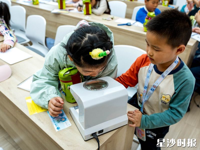 孩子们对着人民币票据鉴别仪仔细寻找水印。 孩子们对着人民币票据鉴别仪仔细寻找水印。