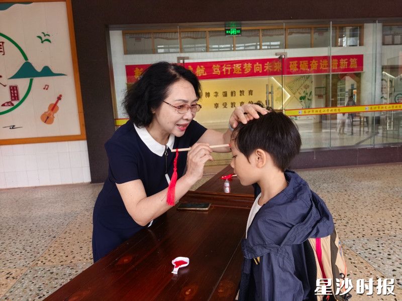 图为长沙市湘龙小学老师手执朱砂,为学童点上朱砂痣,寄托开启智慧、明理向善的美好期许。