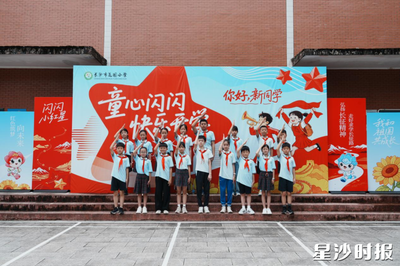长沙市花园小学开学现场,少先队员们在红色主题背景板前整齐列队敬礼,红色教育浸润开学第一课。
